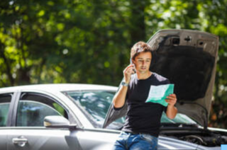 Picture of Guy leaning on car with hood open holding paper while on the phone