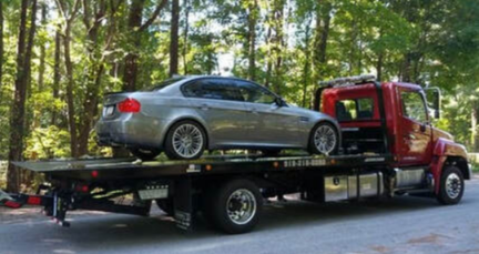 Picture of Silver Car on Flat Bed Tow Truck Driving through forested road