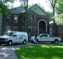 Service van and pickup truck parked in front of a large, traditional brick house