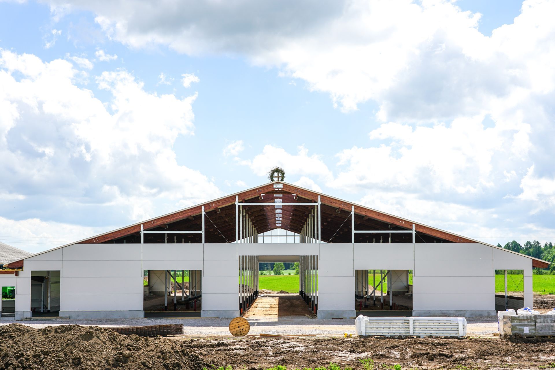White building under construction with a large open entryway and open roof frame, blue sky.