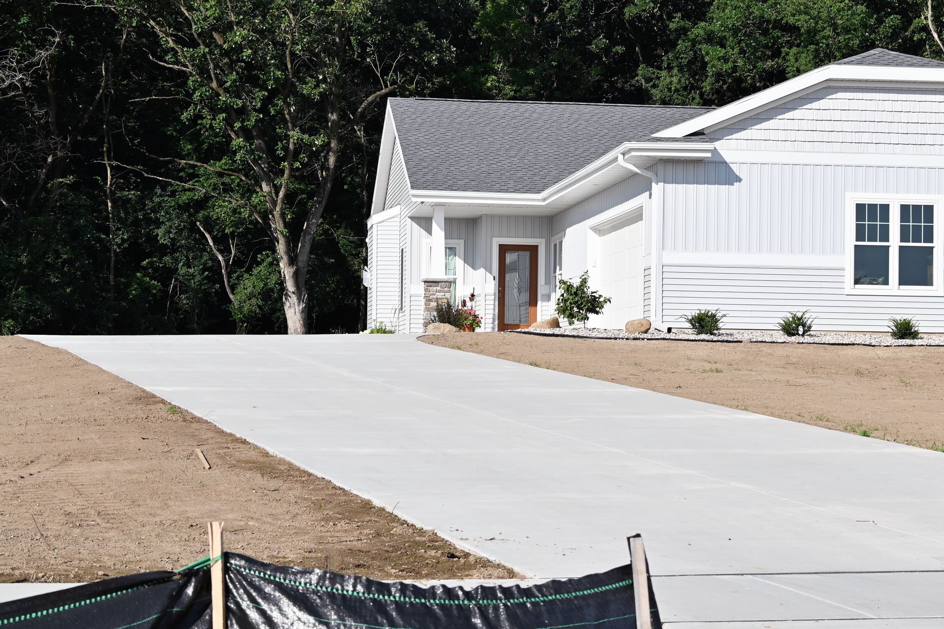 Long concrete driveway leading to a light blue house with a gray roof; trees in the background.