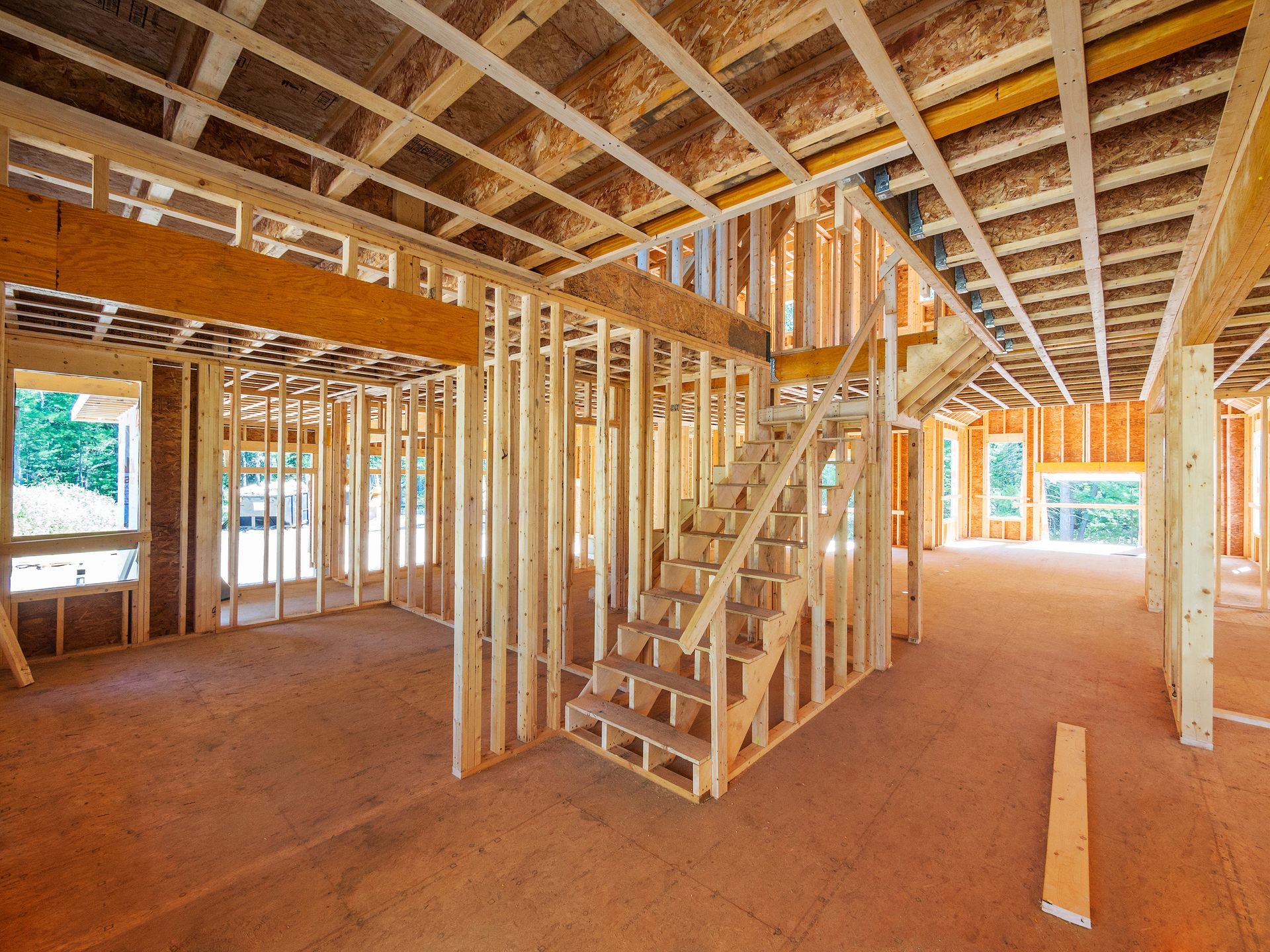 Interior of a house under construction; wooden framing, unfinished floors, and a staircase.