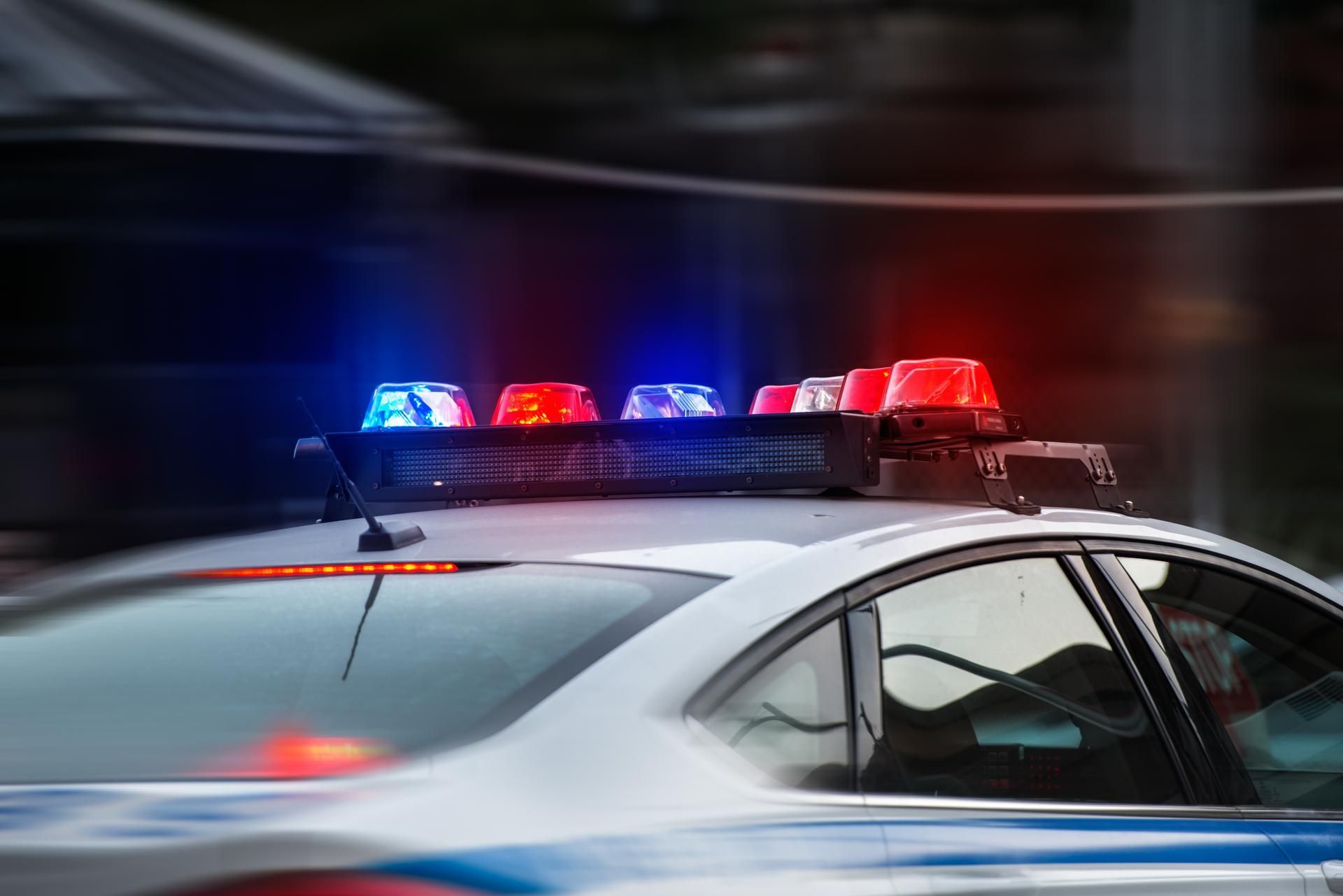 Police car with flashing red and blue lights, blurred background suggesting motion.