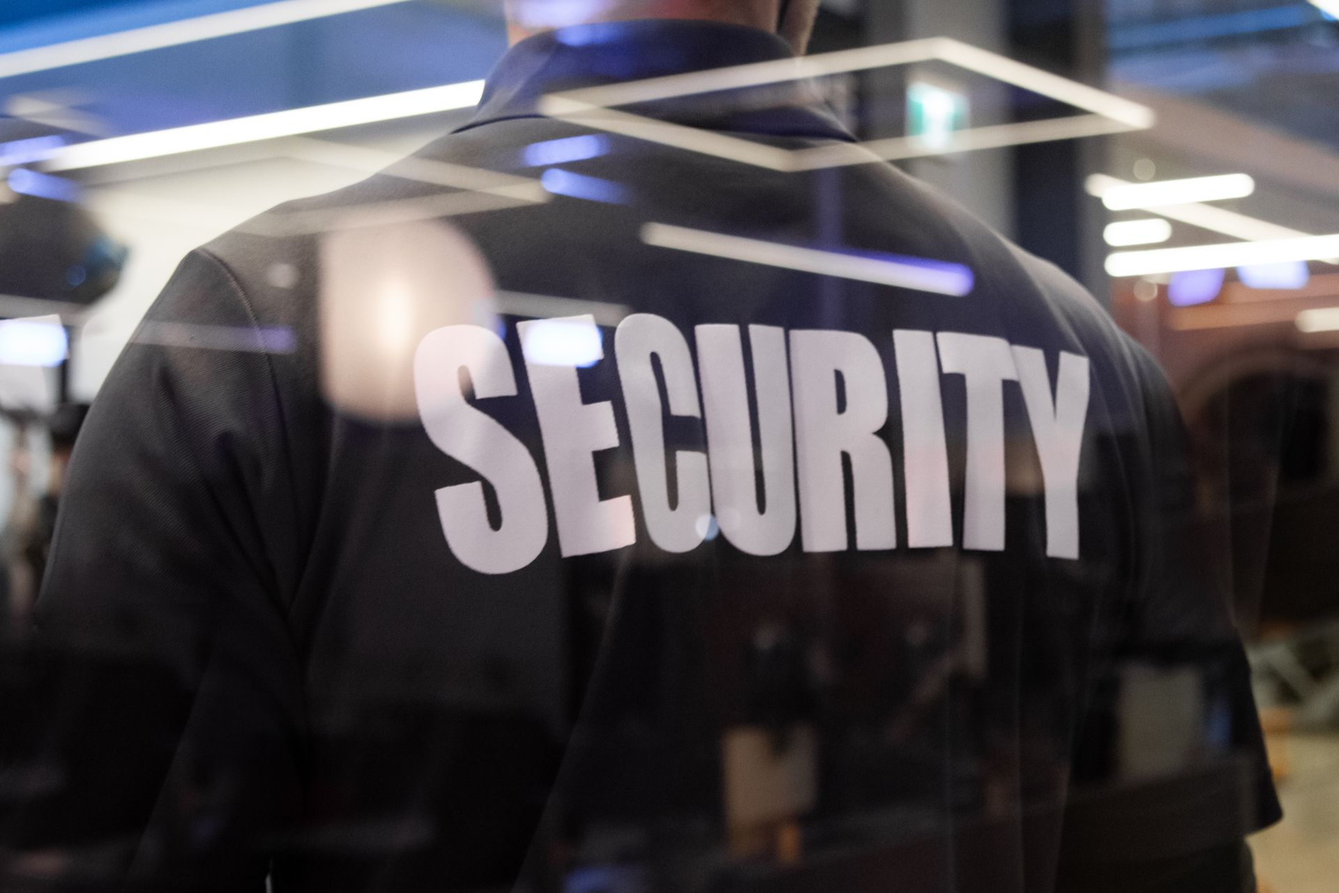 A security guard standing inside a commercial building nearby the window reflecting light