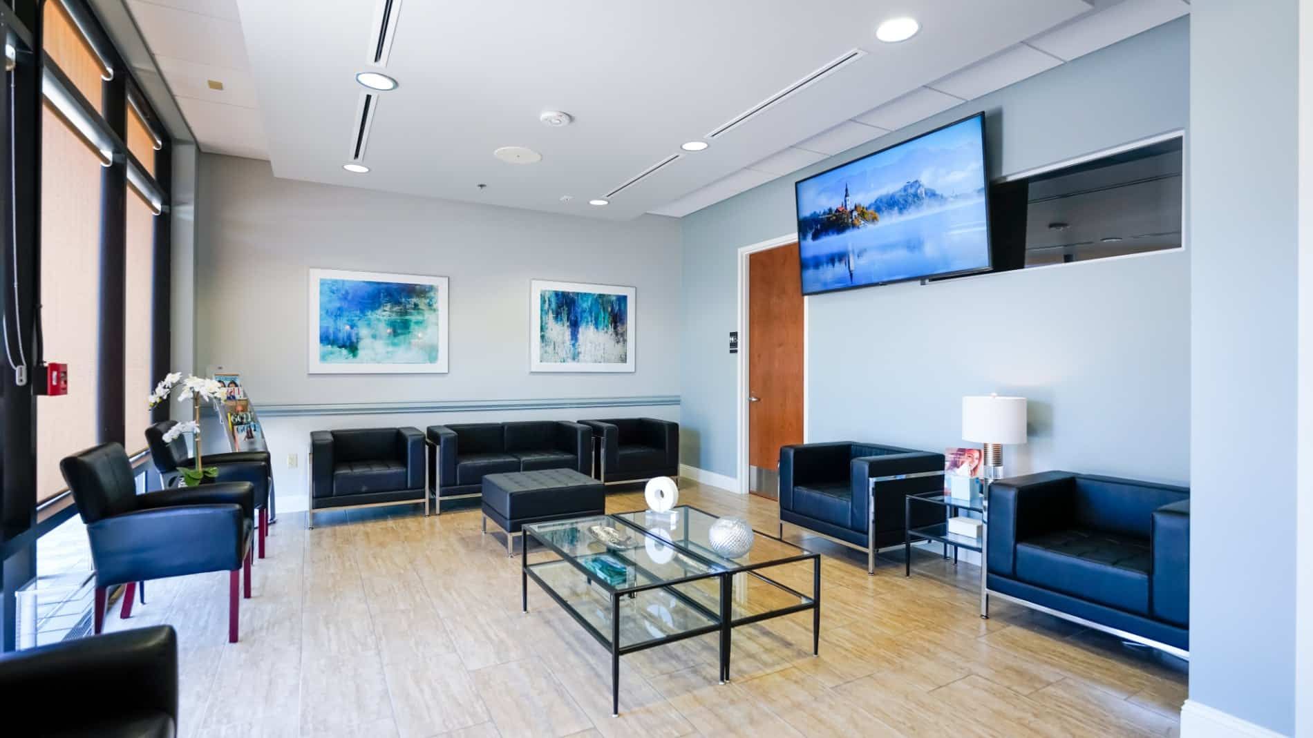 A waiting room with chairs , a coffee table and a flat screen tv.