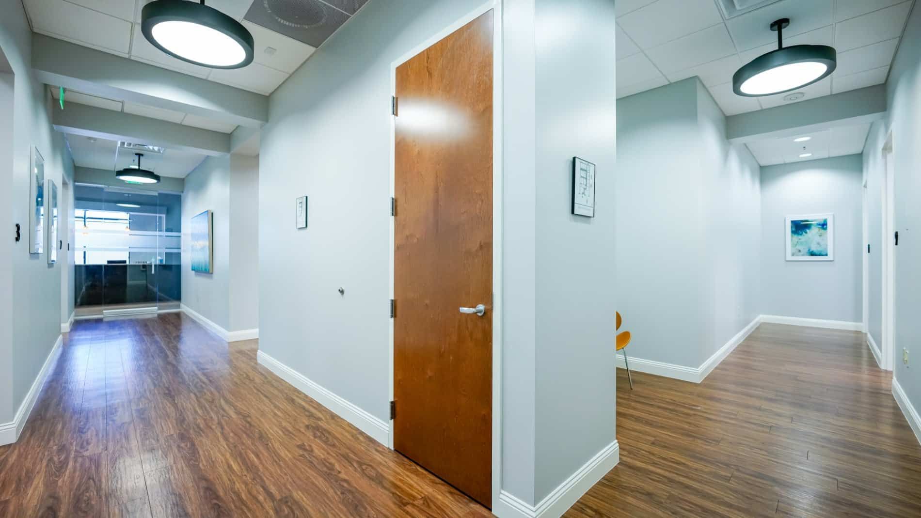 A long hallway with wooden floors and a wooden door in a building.