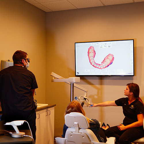 A woman is sitting in a dental chair while a man stands behind her