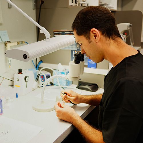 A man in a black shirt is looking through a microscope