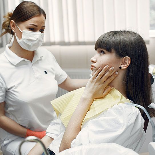 A woman is sitting in a dental chair with a dentist wearing a mask.