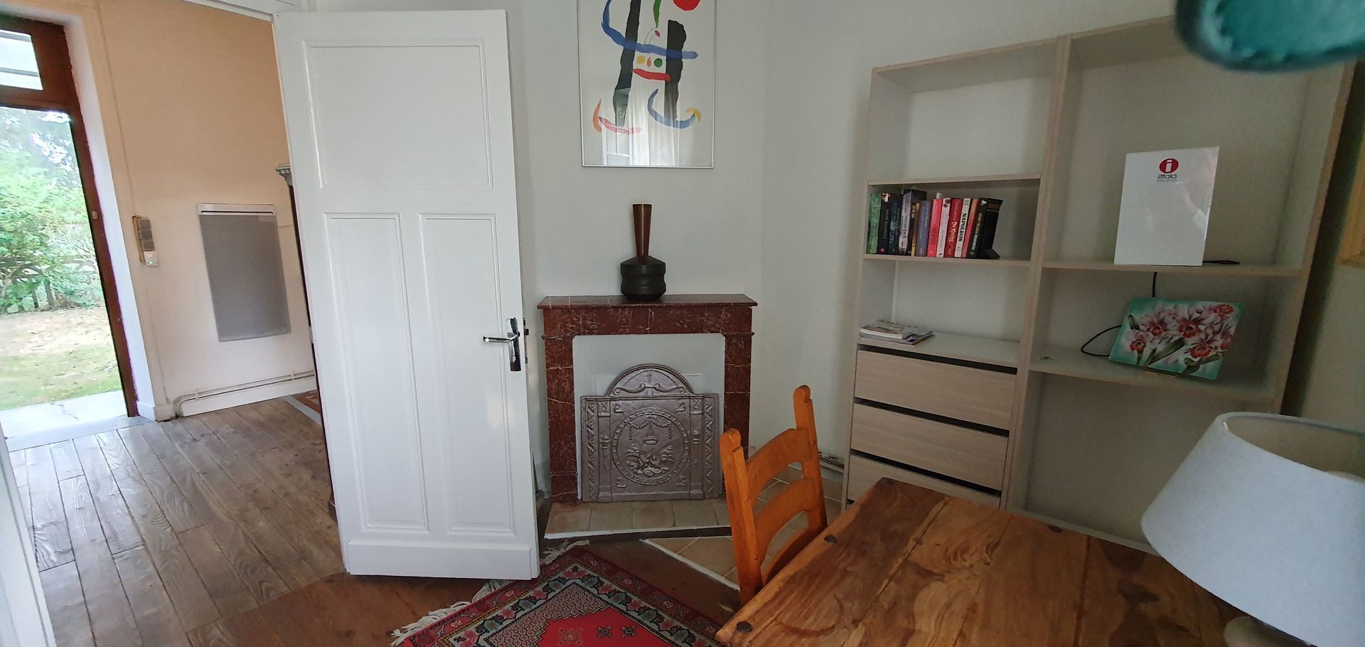 Een kamer met een tafel en stoelen, boekenkast en haard met stenen schouw