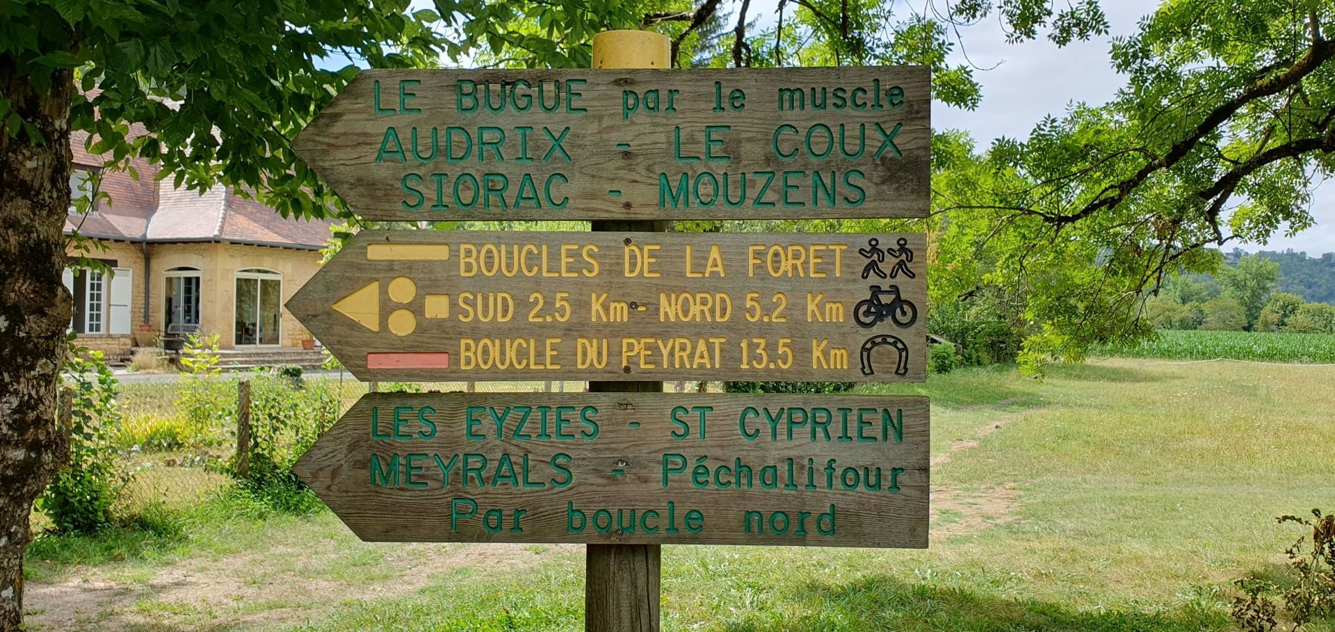 Wooden trail sign with directions in French, green field, and house in the backgroun