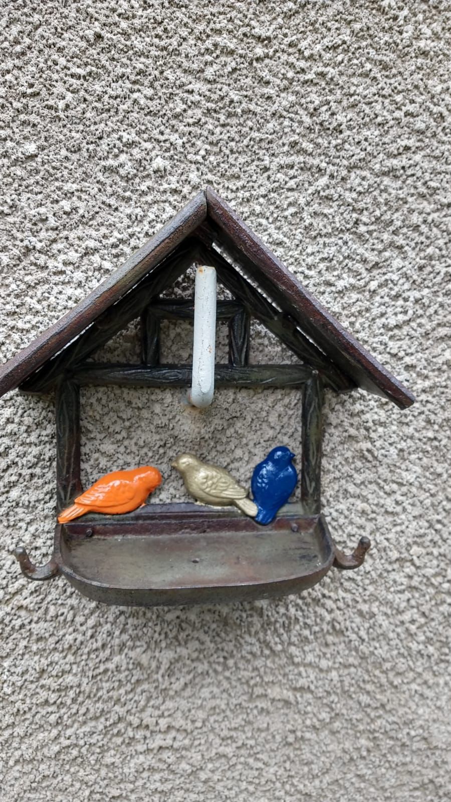 Aan de muur hangt een voederbak met drie gekleurde vogels.