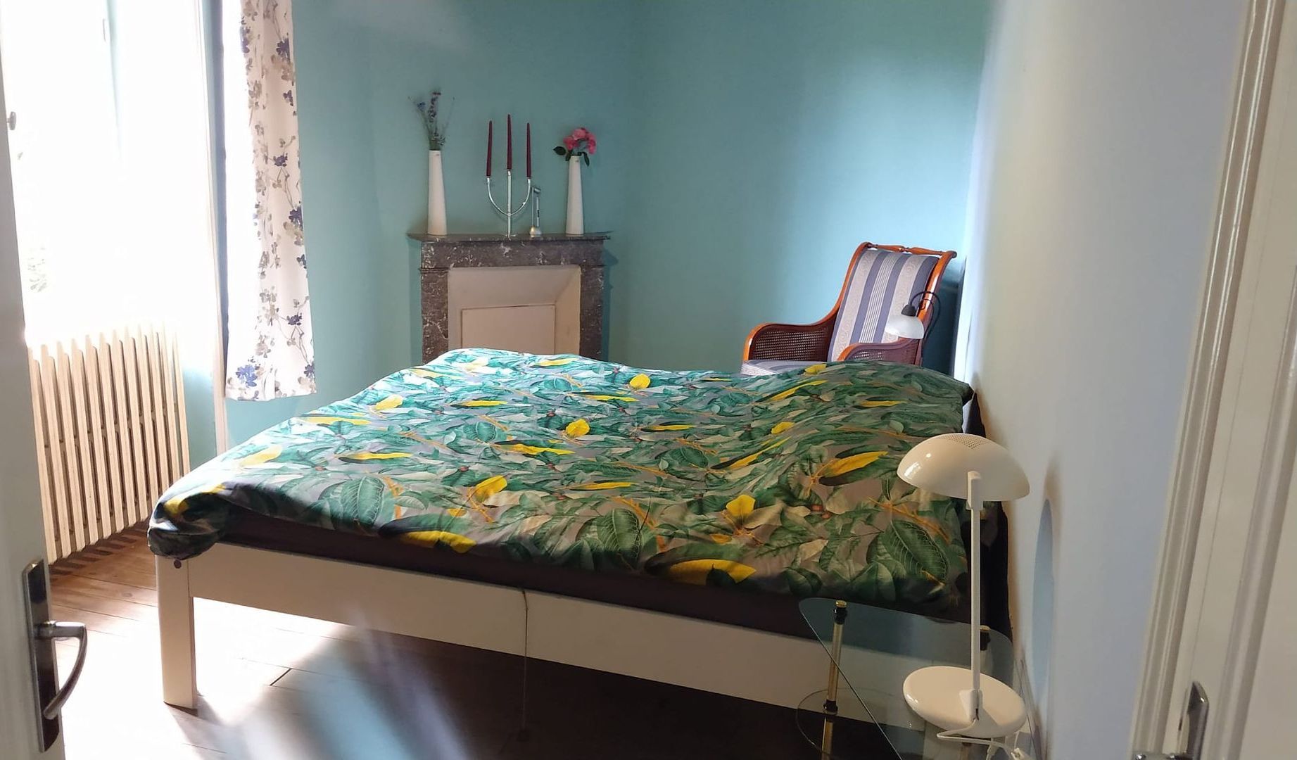 Een slaapkamer met een bed, een stoel en schouw met bloemen
