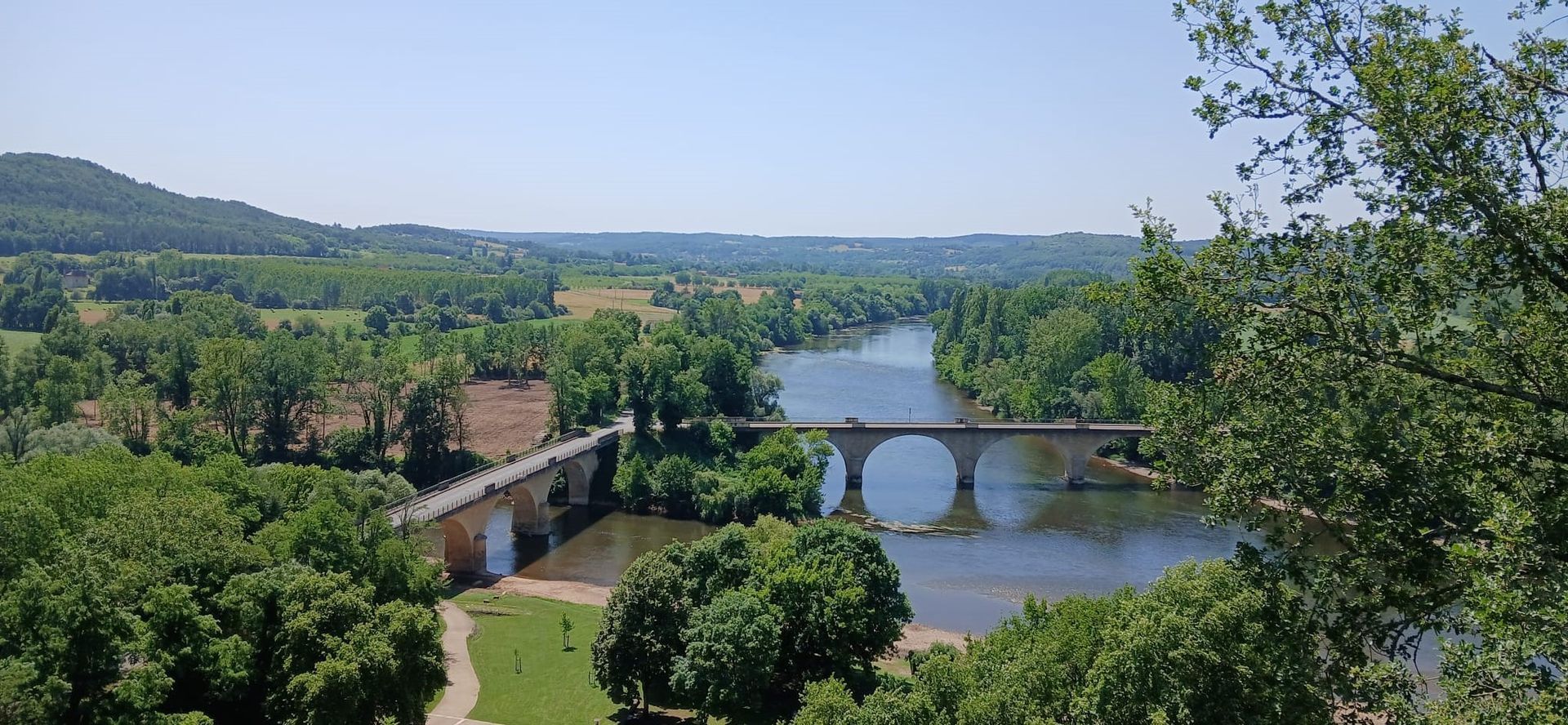 Scenic view of a river with stone bridges and lush green trees under a clear sky.