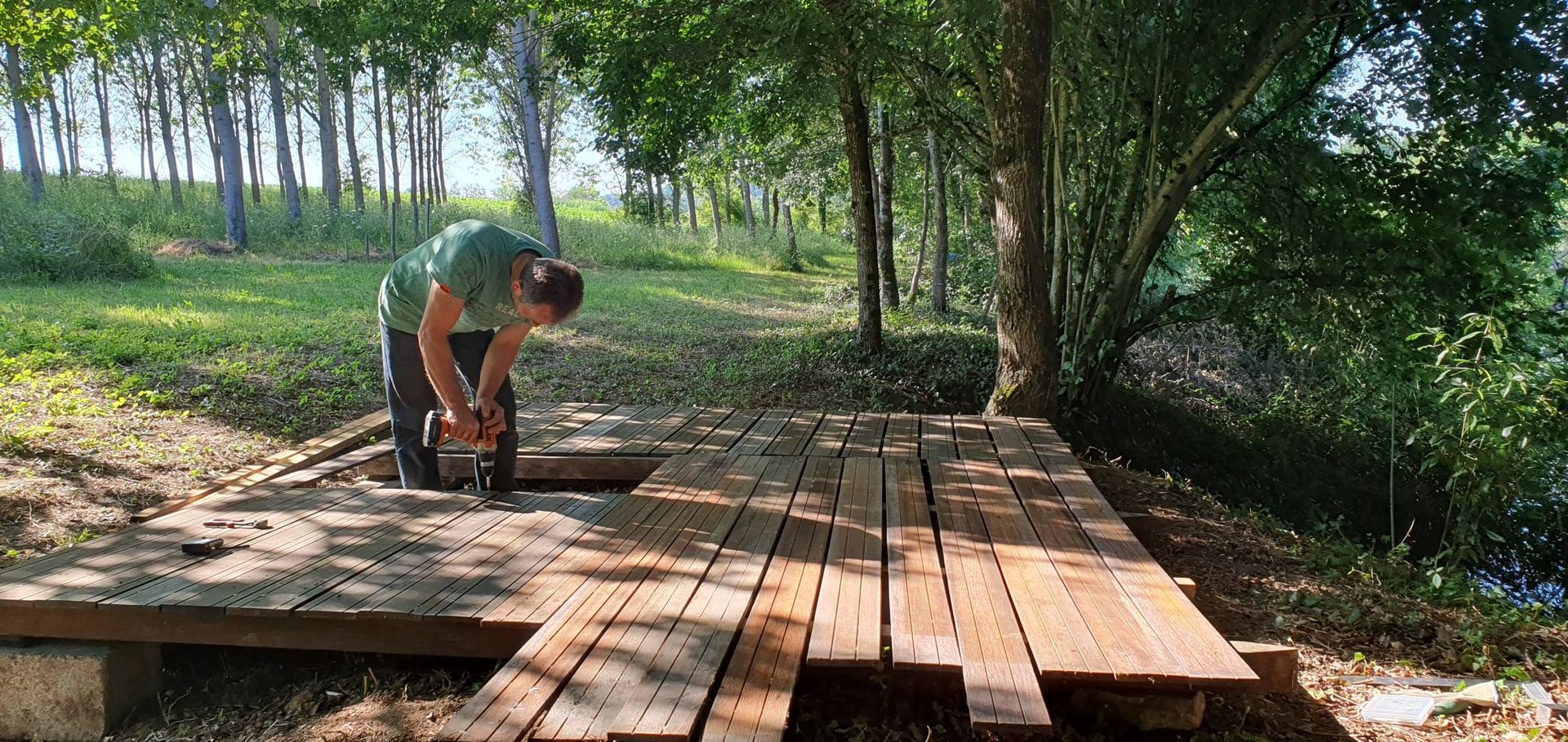 A person using a chainsaw to cut wood on a wooden deck in a forest.
