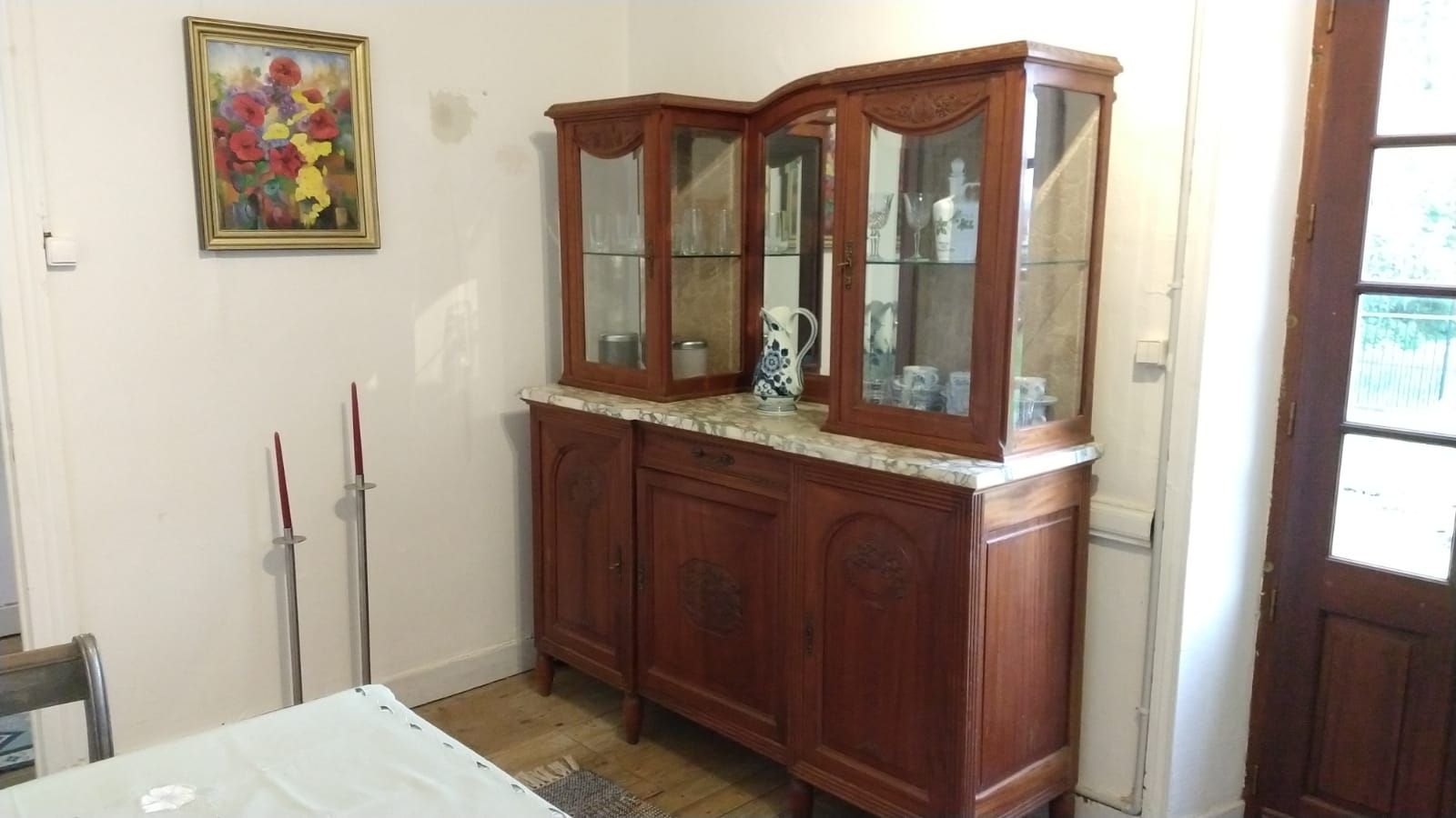 Een kamer met grote houtkachel, tafel, stoelen en een broquante kast