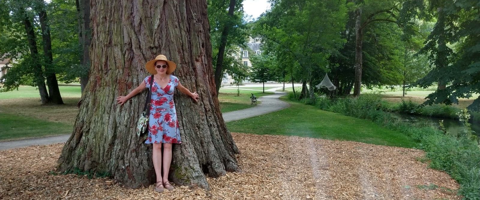 Woman in hat embraces large tree in park.