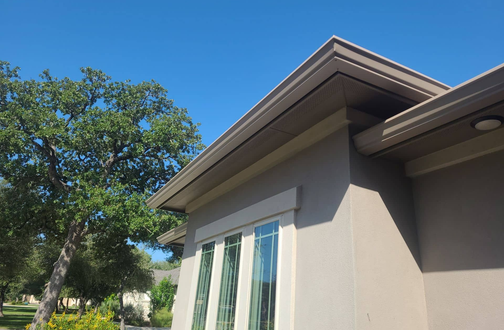 Corner of a house with a brown roof and a blue sky in the background.