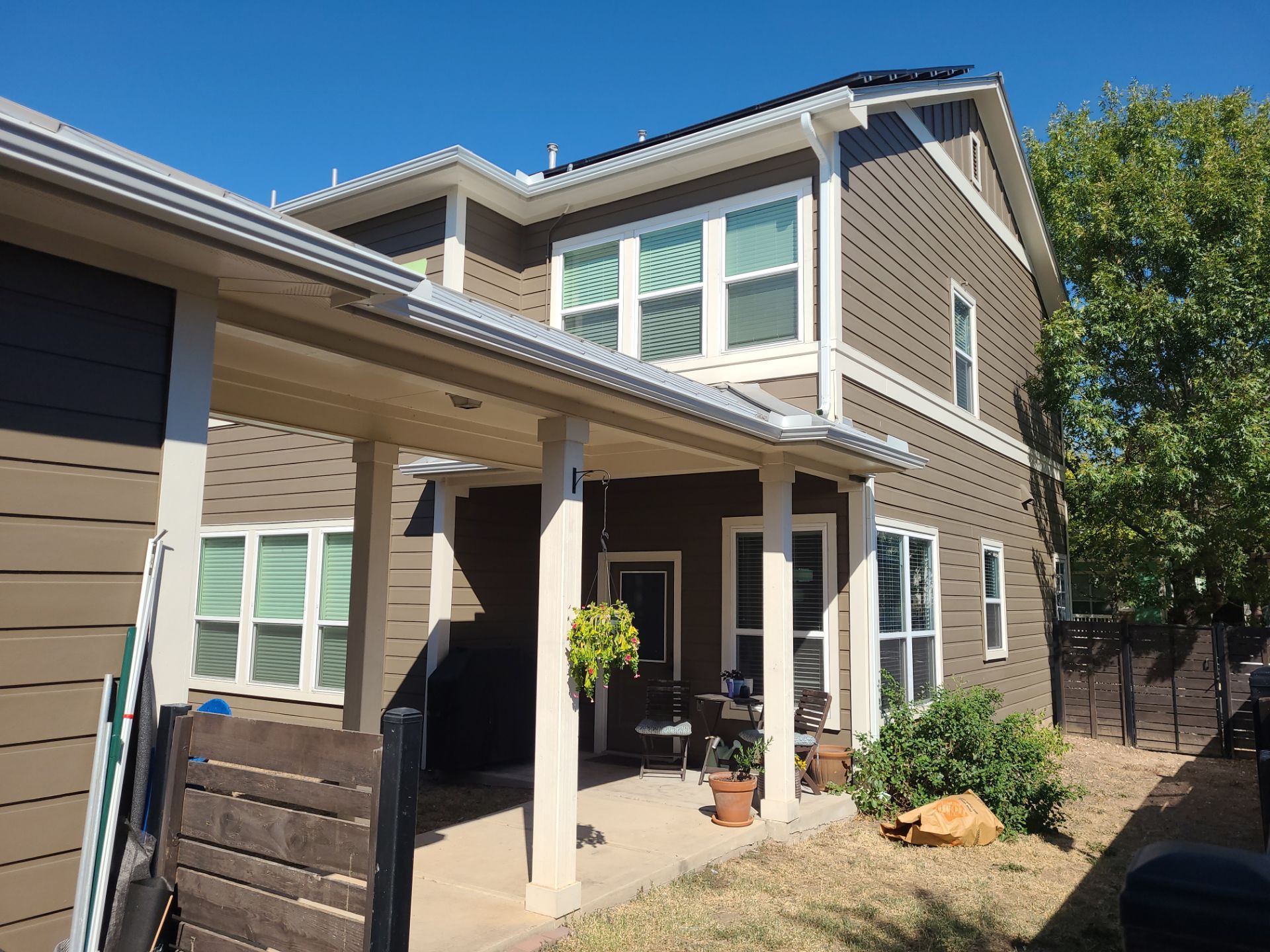 Brown and white two-story house with covered porch, guttering, and a sunny, outdoor setting.