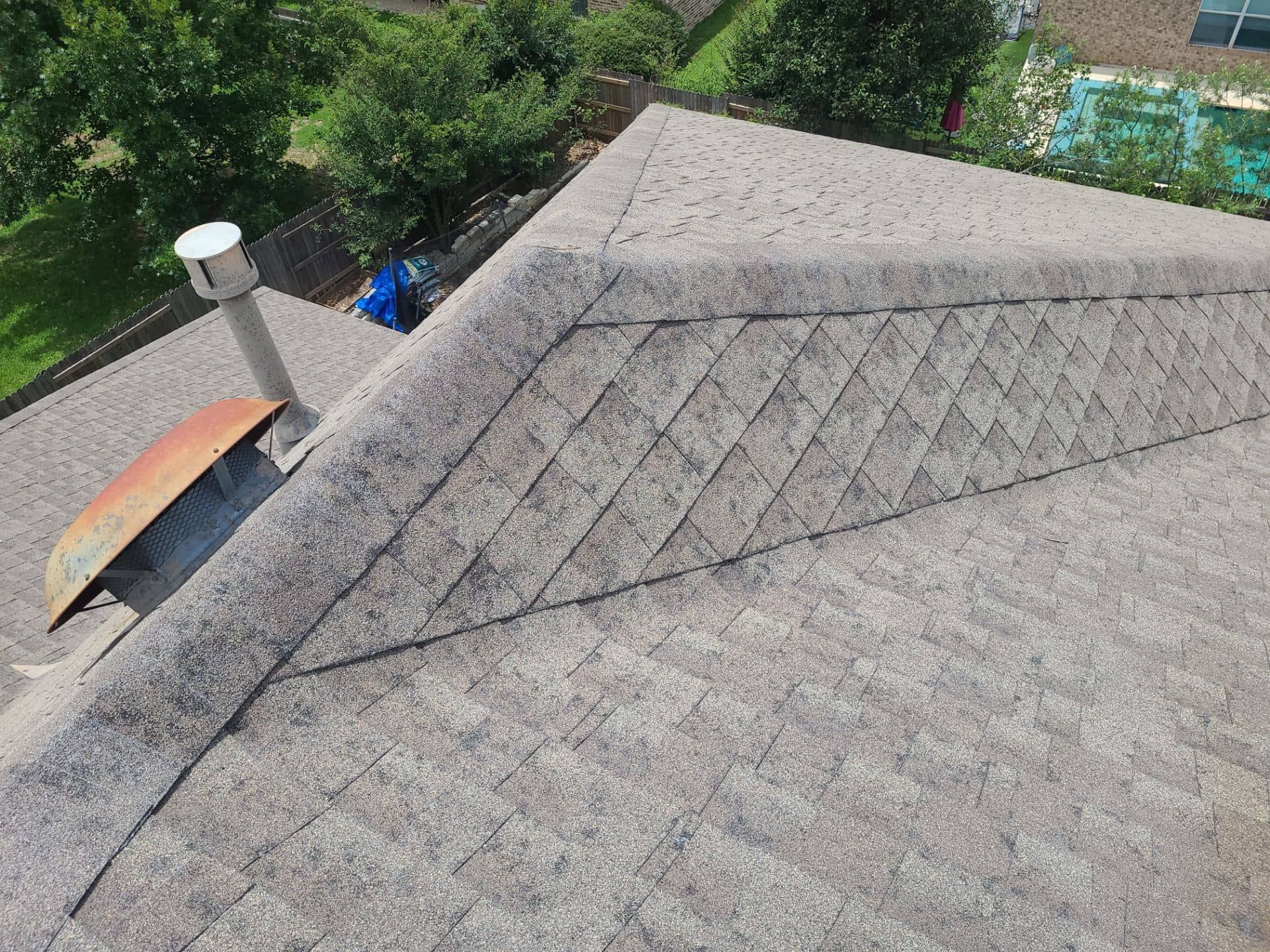 View of a weathered asphalt shingle roof with a chimney and ridge cap.