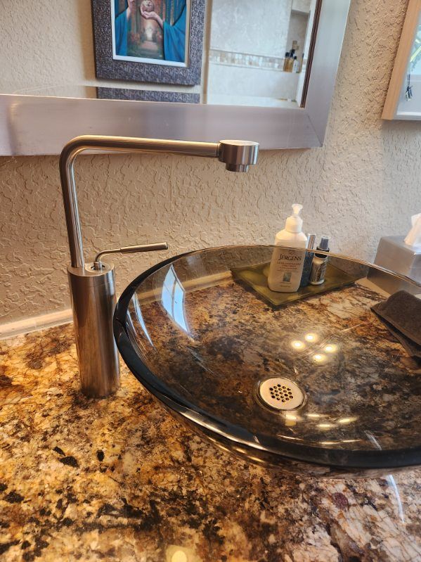 Modern bathroom sink with glass bowl, brushed nickel faucet, and soap dispenser on speckled granite countertop.