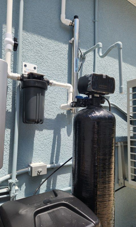 Water filtration system mounted on a blue wall. Includes filter, UV light, and water softener.