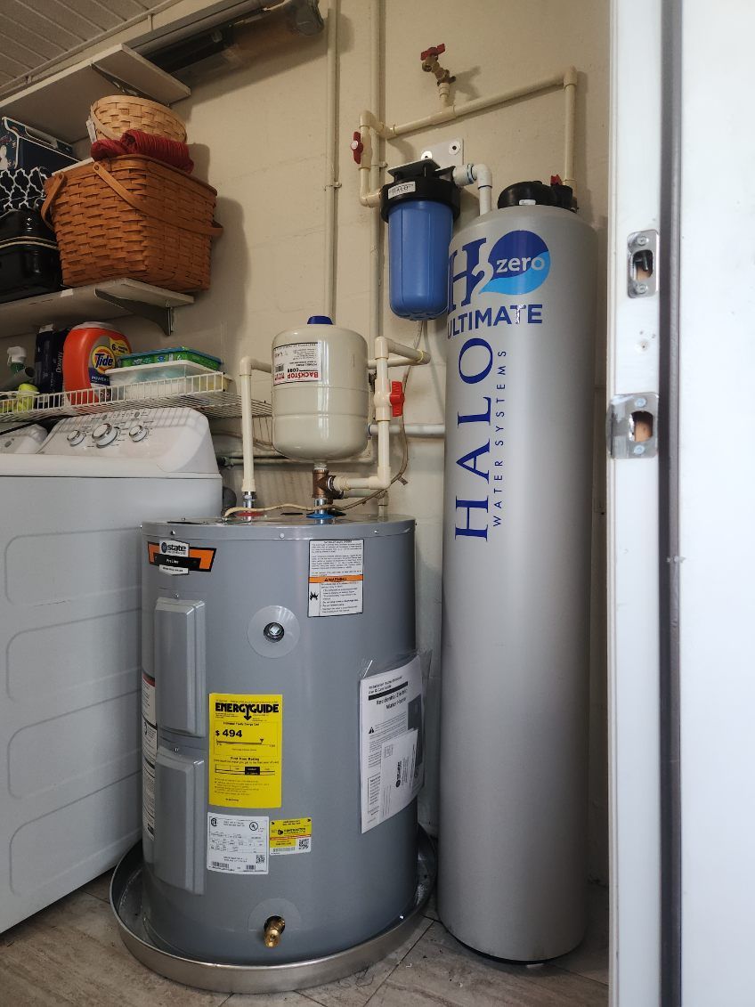 A laundry room with a water heater, water softener, filter, and washing machine.