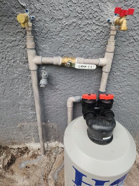 Plumbing system with a water filter and valves attached to a gray stucco wall.