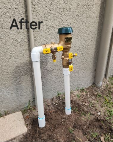 A backflow preventer and PVC pipes in front of a wall, labeled 