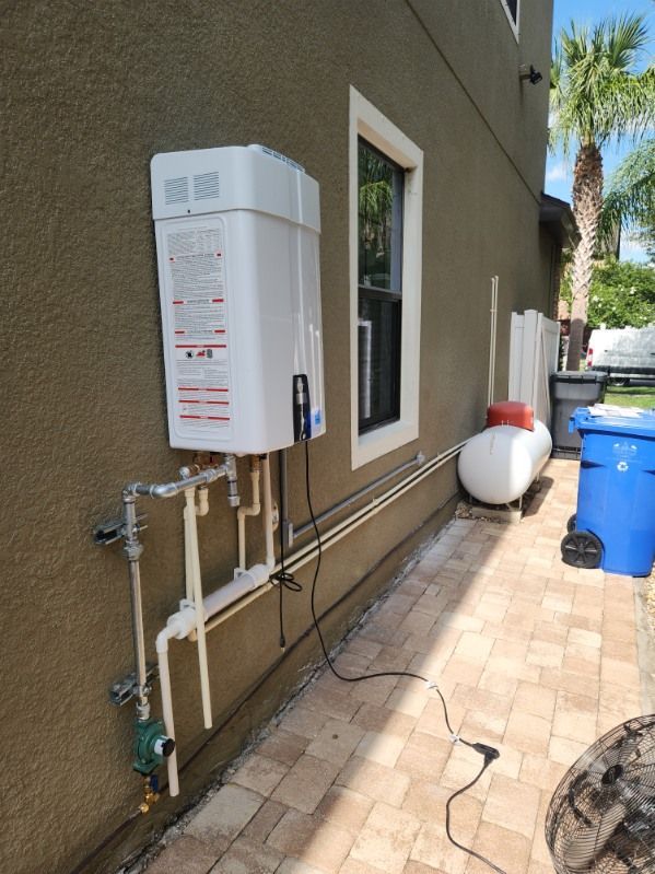 White tankless water heater mounted on a brown wall next to a window and propane tank.