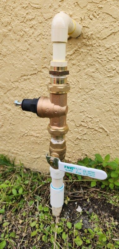 Plumbing setup with a pressure regulator, shutoff valve, and PVC pipes attached to a stucco wall.
