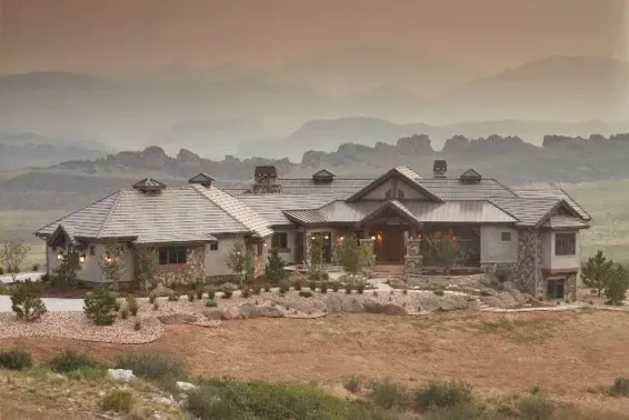 A large house is sitting on top of a hill with mountains in the background.