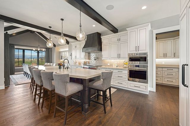 A kitchen with white cabinets , stainless steel appliances , hardwood floors and a large island.