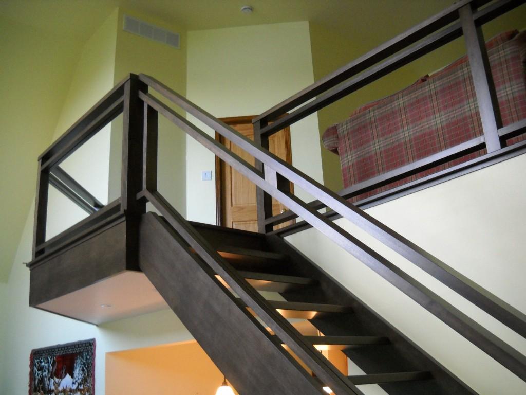 Un escalier en bois avec une rampe en verre menant au deuxième étage