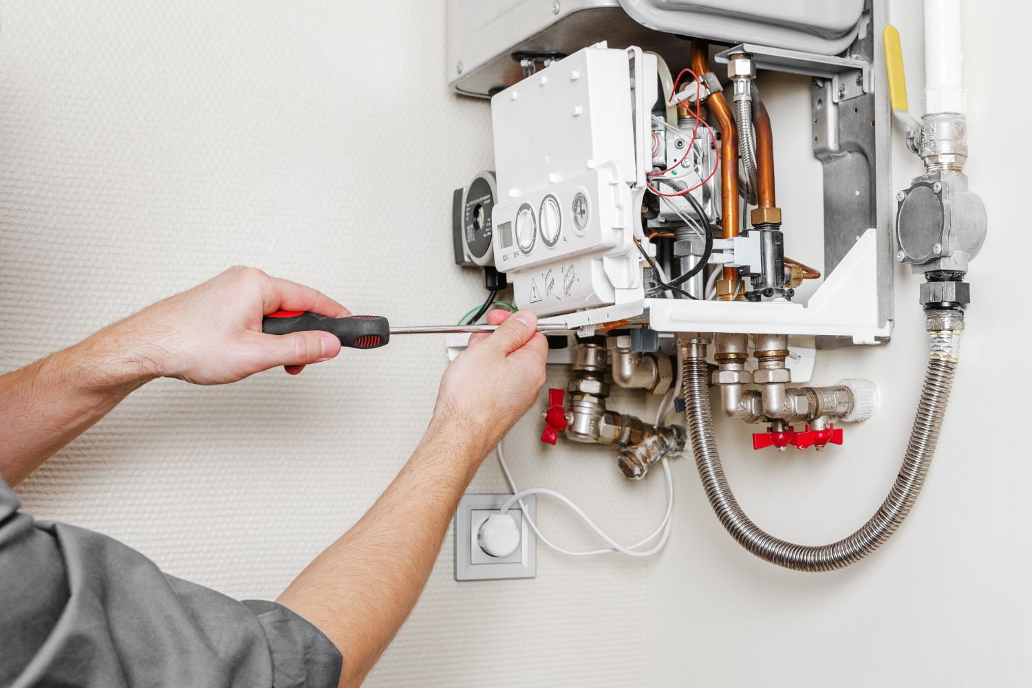 A man is fixing a boiler with a screwdriver.