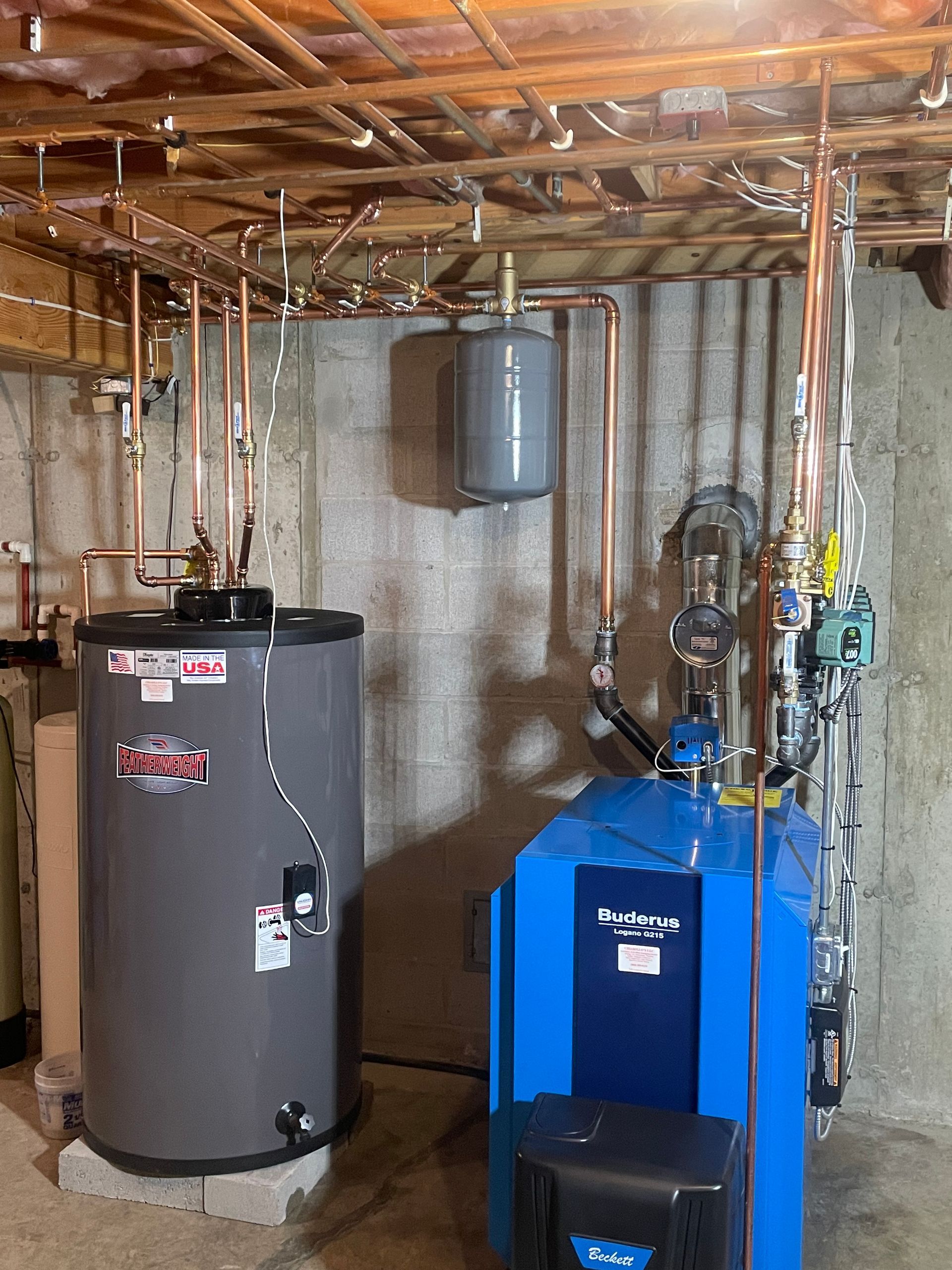 A blue water heater is sitting next to a gray water heater in a basement.