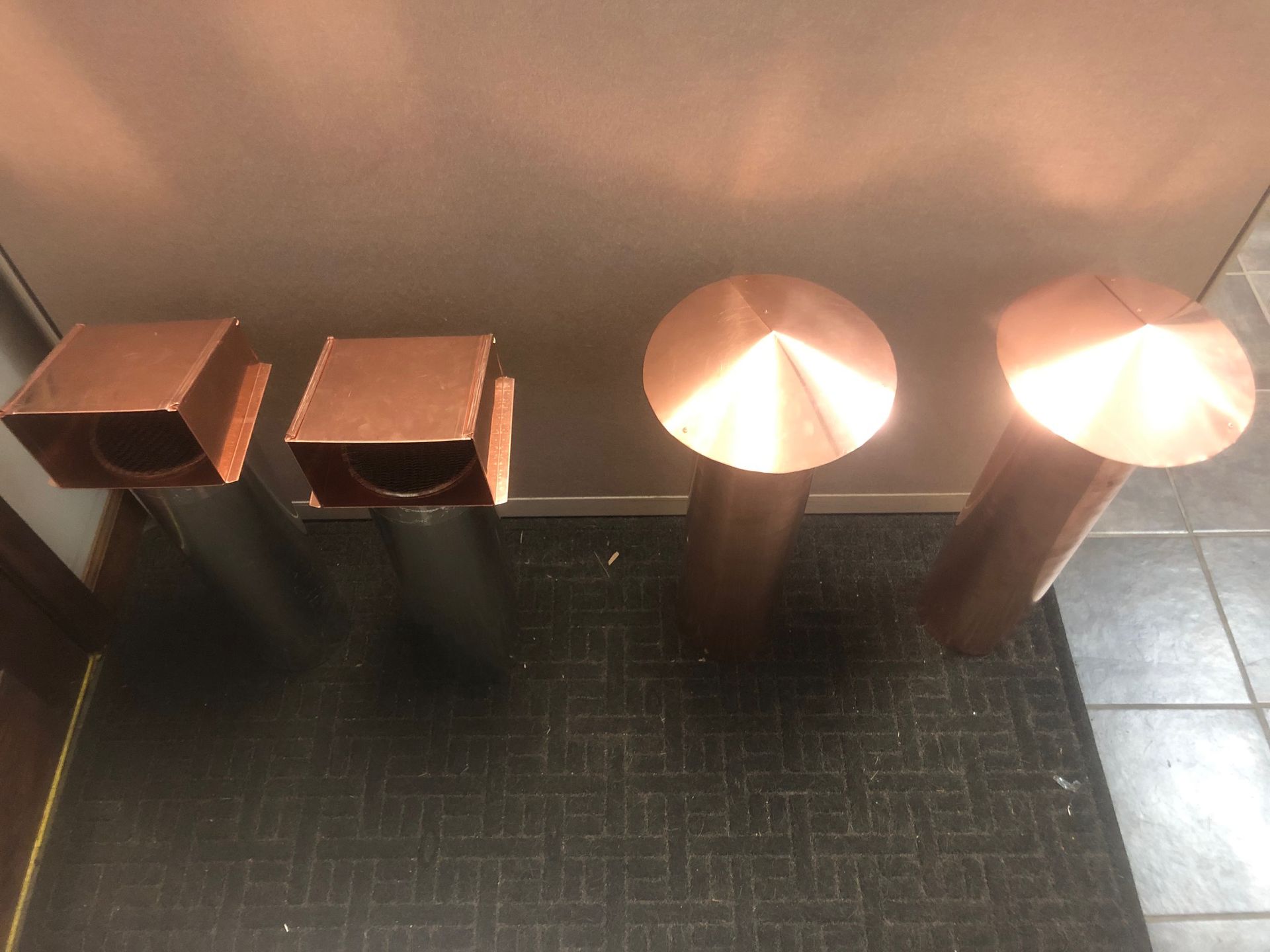 Three copper pipes are sitting on a tiled floor