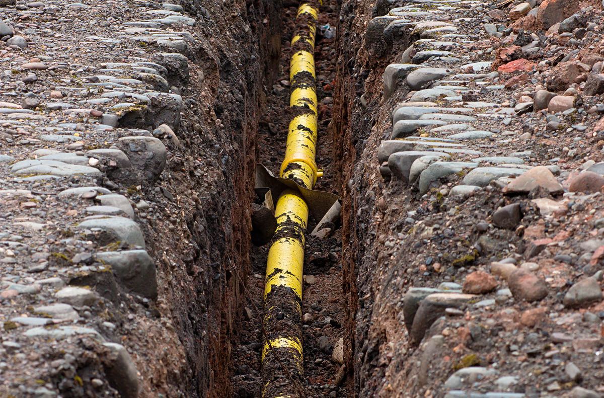 A yellow pipe is being installed in a trench.