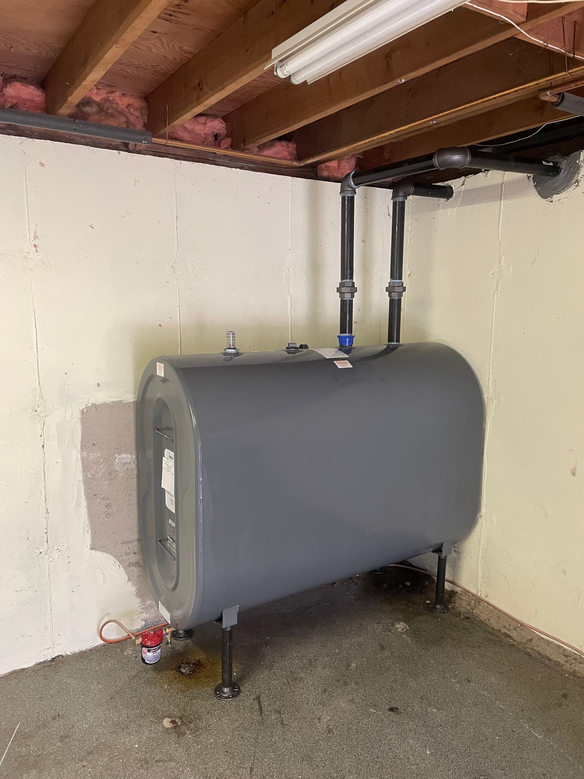 A large gray tank is sitting in a basement under a wooden ceiling.