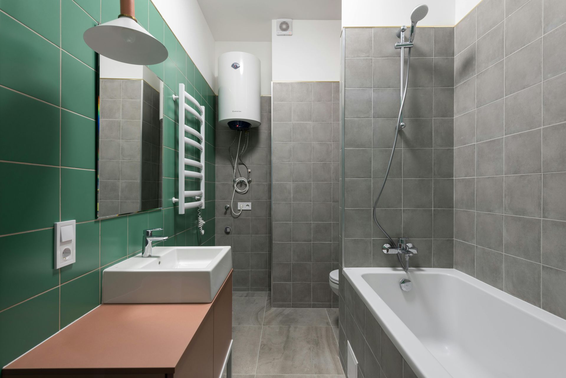 Modern bathroom with green and gray tiles, white fixtures, and a brown vanity.