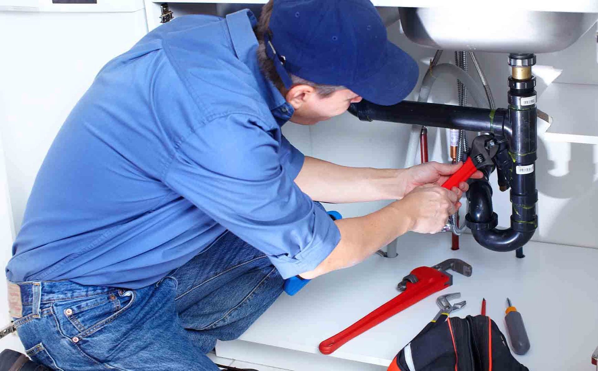 a man in a blue shirt is working on a pipe under a sink