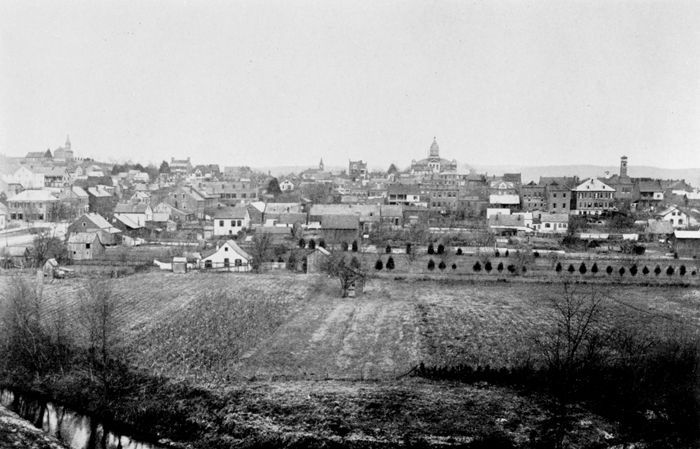 A black and white photo of a small town with a river in the foreground.