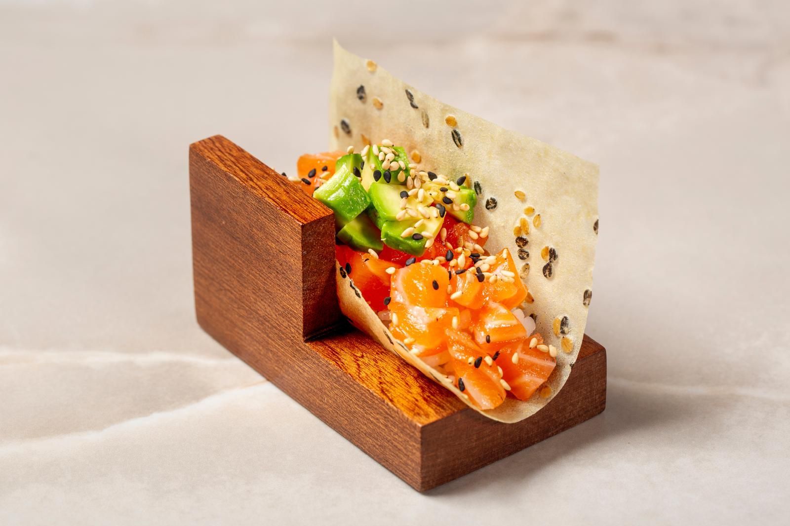Un taco con salmone crudo e avocado, guarnito con semi di sesamo