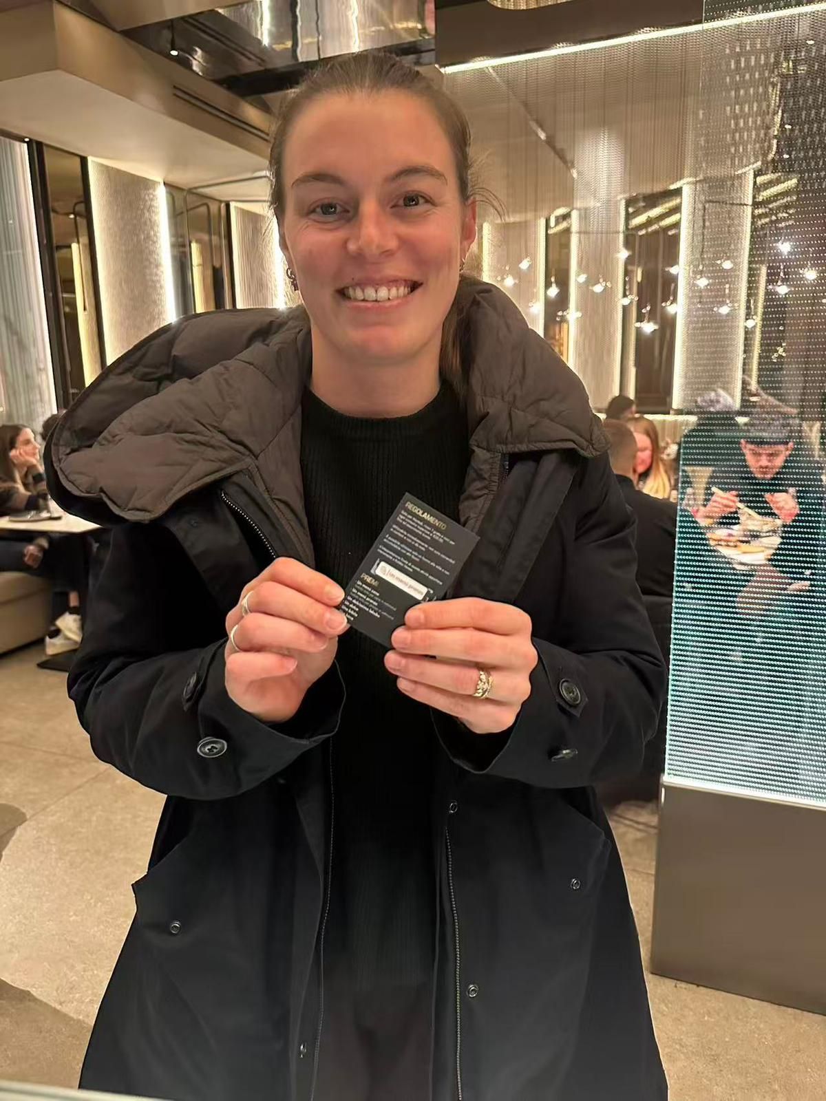 In un ristorante scarsamente illuminato, una persona sorridente con un cappotto scuro tiene in entrambe le mani 