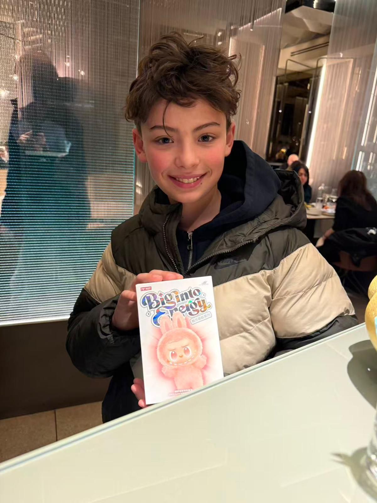 Un giovane sorridente, con indosso una giacca, mostra un piccolo biglietto con l'immagine di un personaggio 