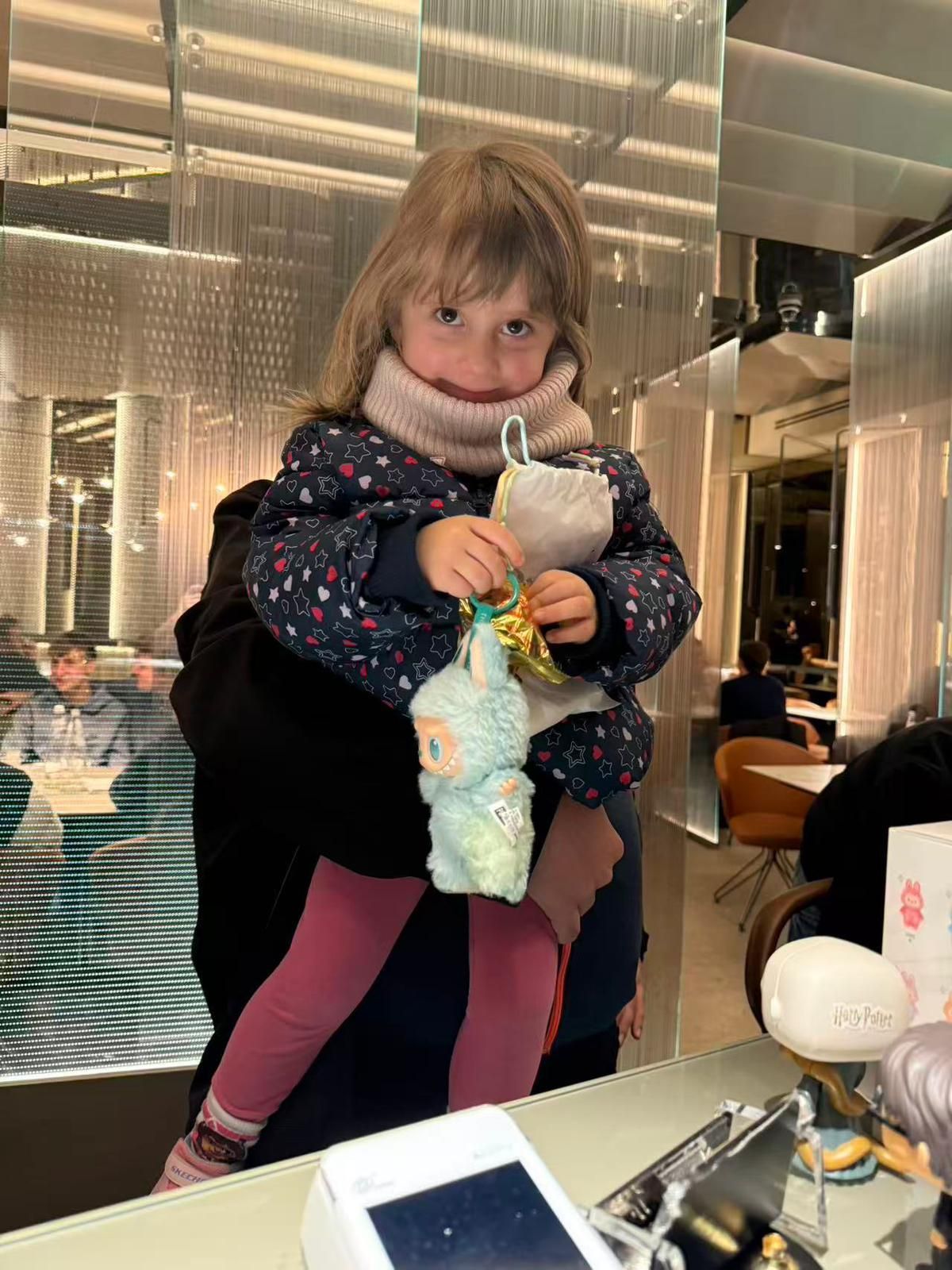 Un bambino con indosso un cappotto e una sciarpa invernali tiene in mano un peluche azzurro mentre