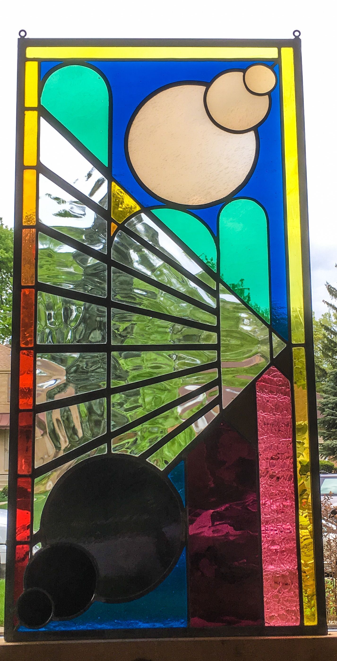 A stained glass window with a colorful design on it is hanging on a window sill.