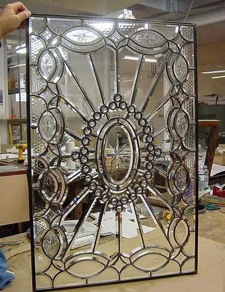 A person is holding a stained glass window in a workshop.