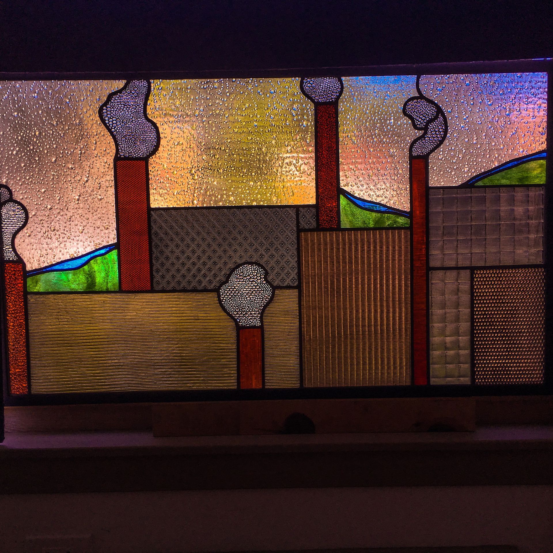 A stained glass window shows a factory with smoke coming out of the chimneys