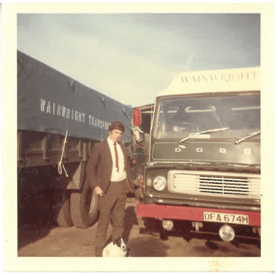 One of the Wainwright Brothers in suit stands by a green truck with 